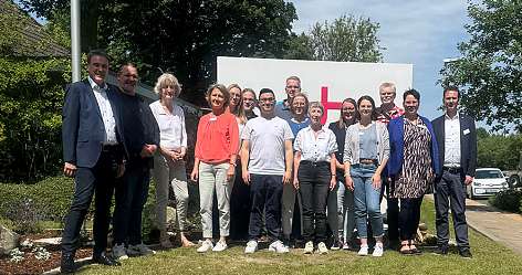 Eine Gruppe von Menschen posiert vor einem großen Schild im Freien.